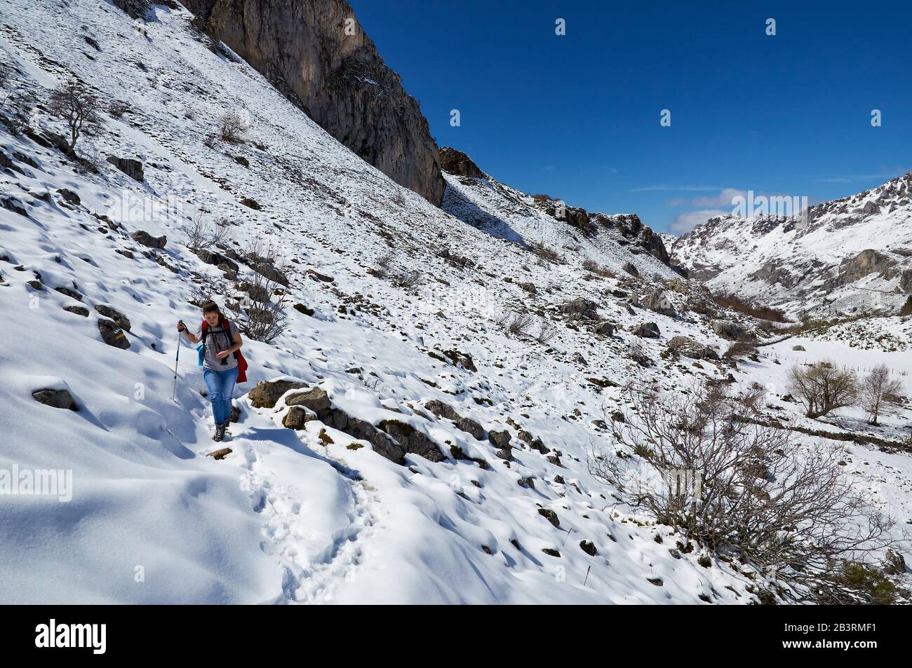 Randonneur féminin dans la piste de randonnée PR.AS-15.1 recouverte de neige avec des montagnes escarpées au loin (Valle del Lago, Soriedo Natural Park, Asturies, Espagne) Banque D'Images