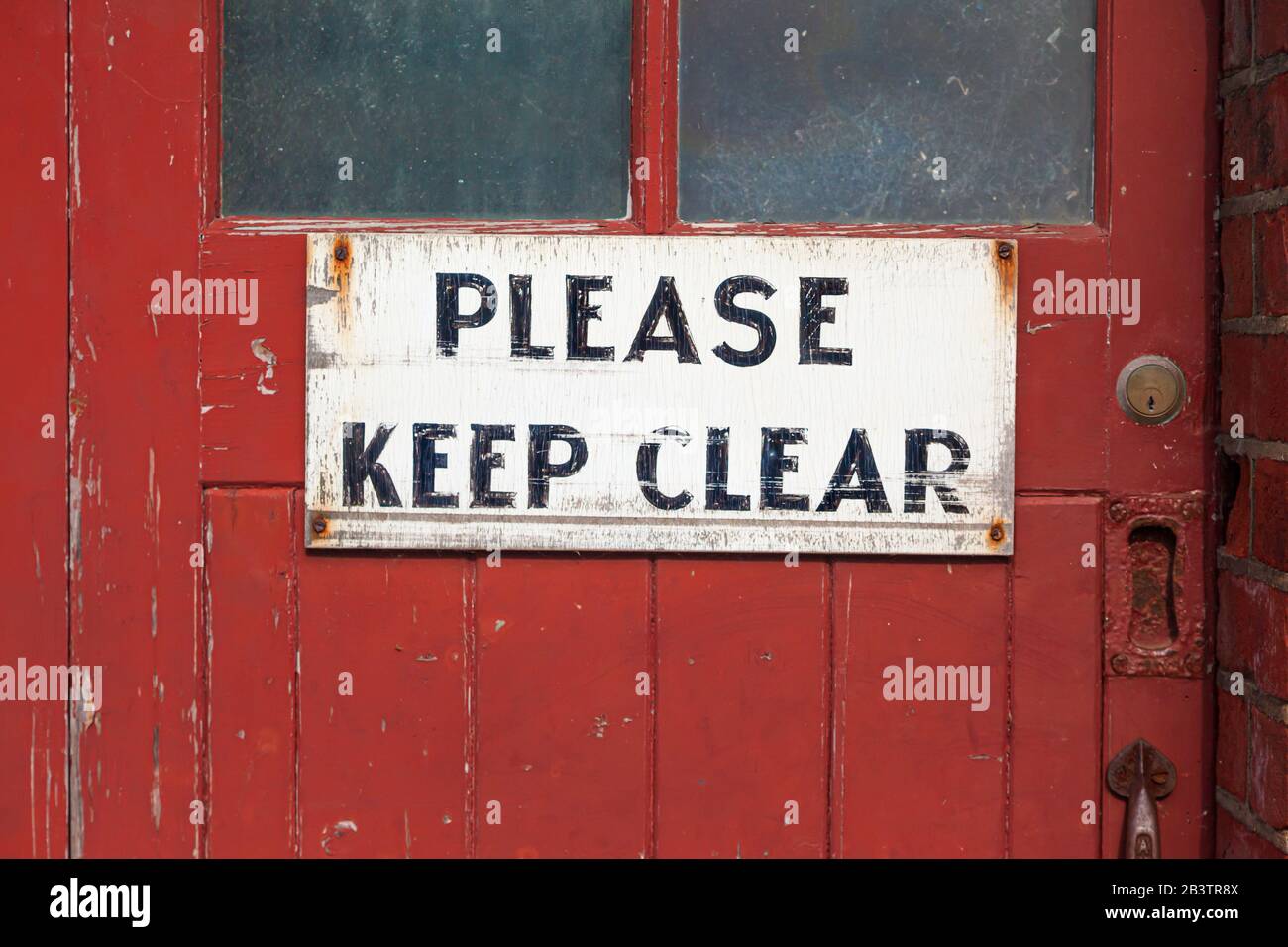 Ancien et usé, peint à la main « Veuillez garder l'étiquette claire » sur l'ancienne porte rouge usée. Banque D'Images