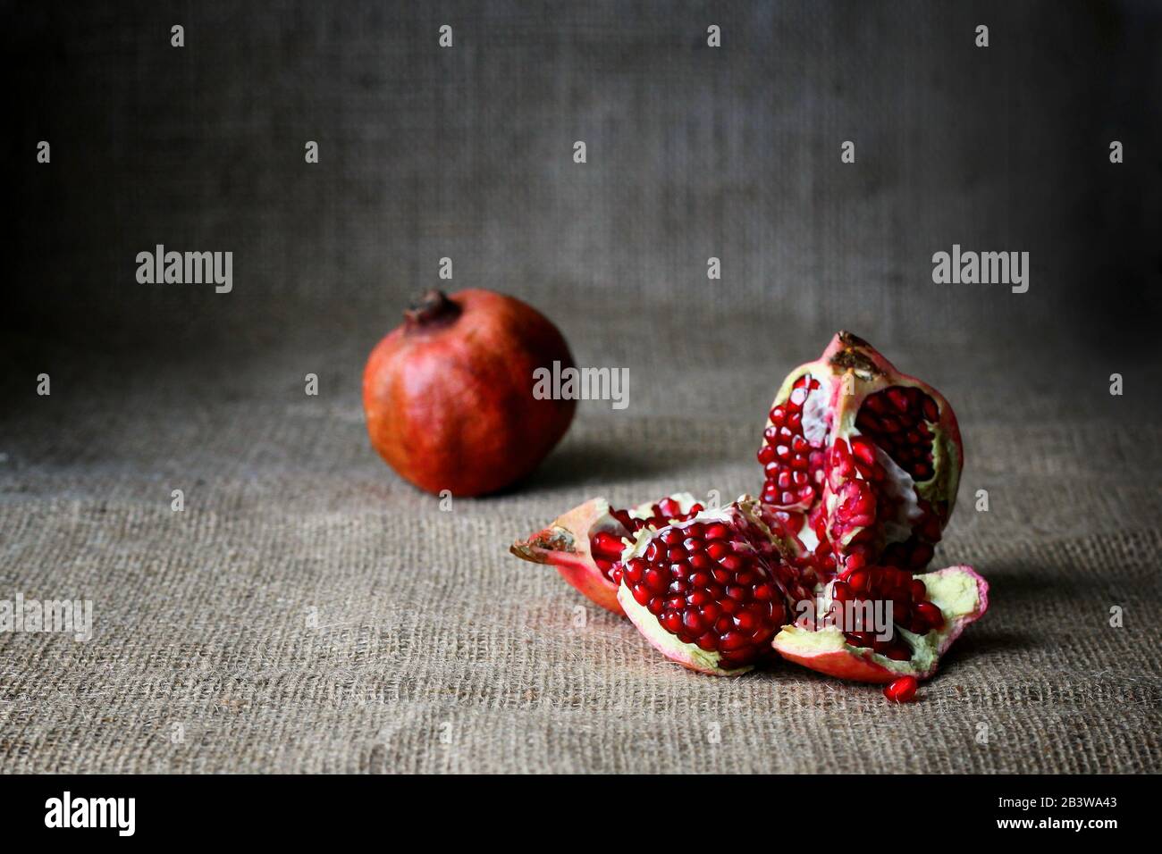 Demi-grenade rouge et grenades crues sur fond brun en toile de fond. Style rustique. Fruits savoureux, queue de vitamine Banque D'Images