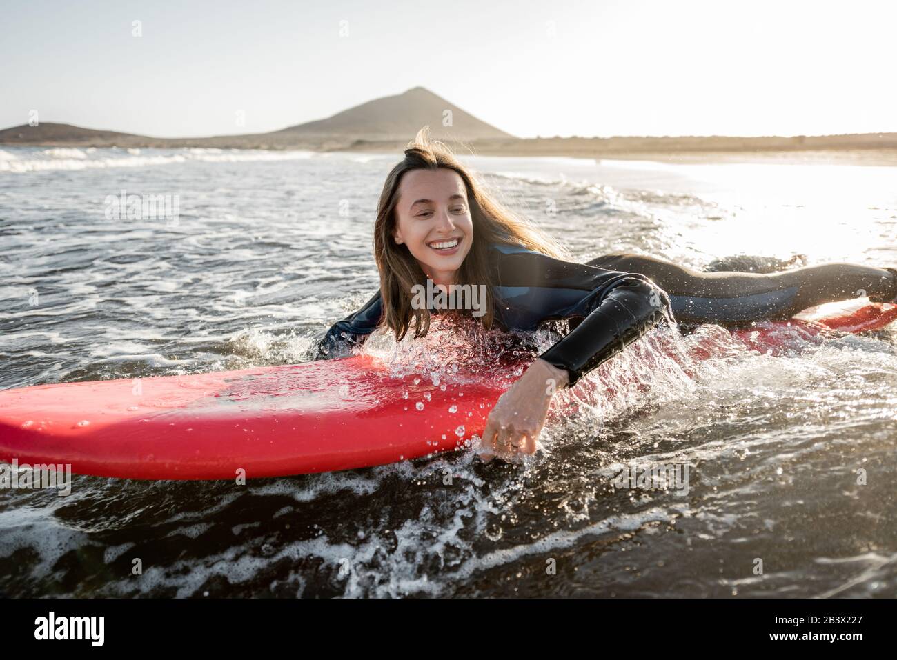 Jeune femme en combinaison qui capte l'écoulement d'eau sur le surf, surfant sur l'océan ondulé pendant un coucher de soleil. Sports nautiques et style de vie actif concept Banque D'Images