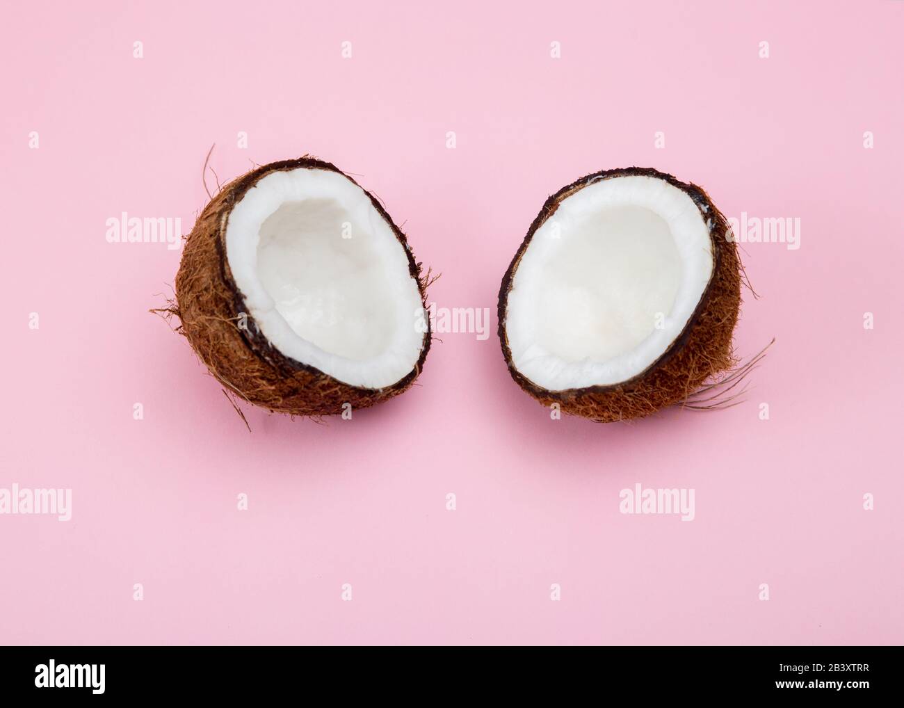 Noix de coco brute fraîche coupée en 2 parties sur un fond rose. Banque D'Images