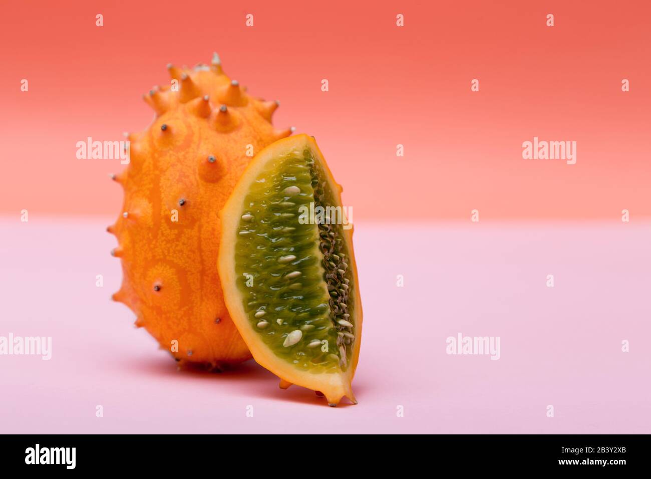 Un Kiwano orange et un demi Kinavo sur fond rose et orange. Banque D'Images