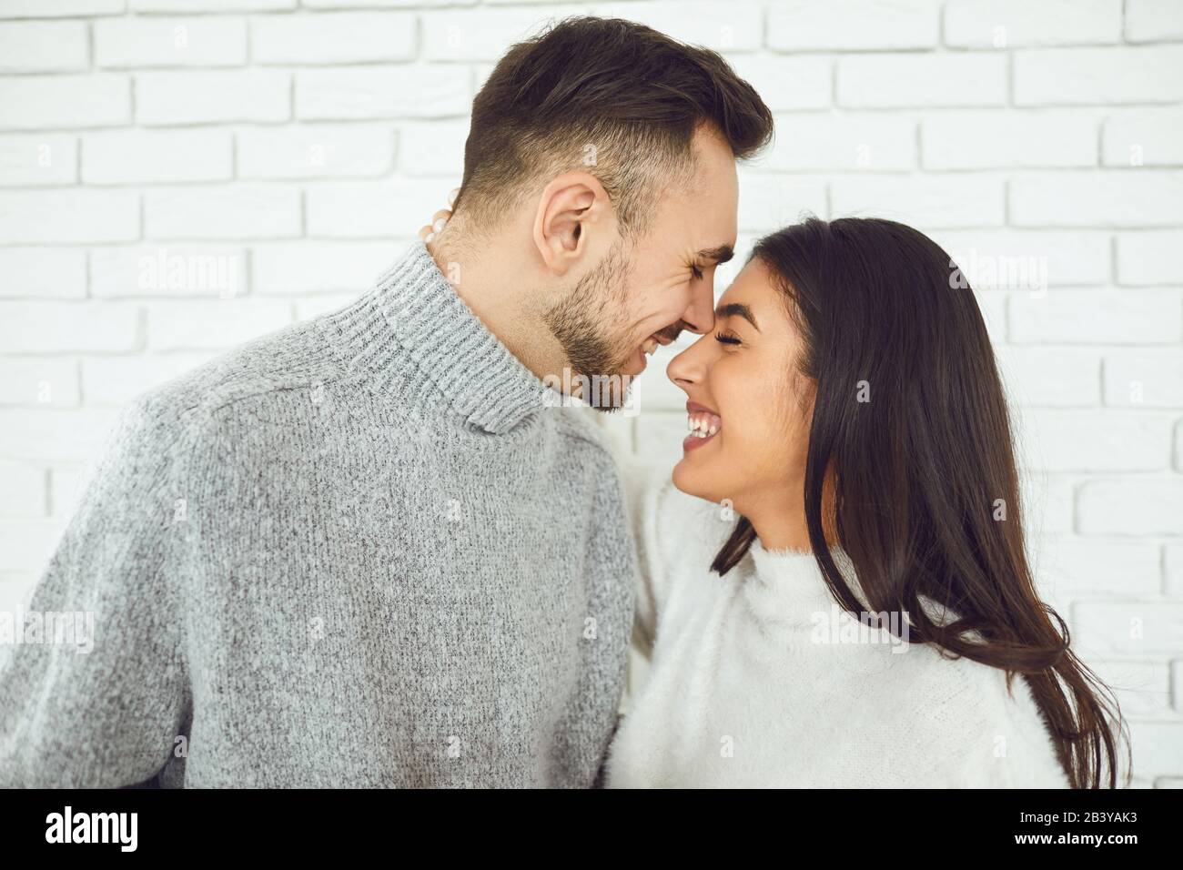 Jeune couple souriant souriant sur un fond de brique blanche Banque D'Images