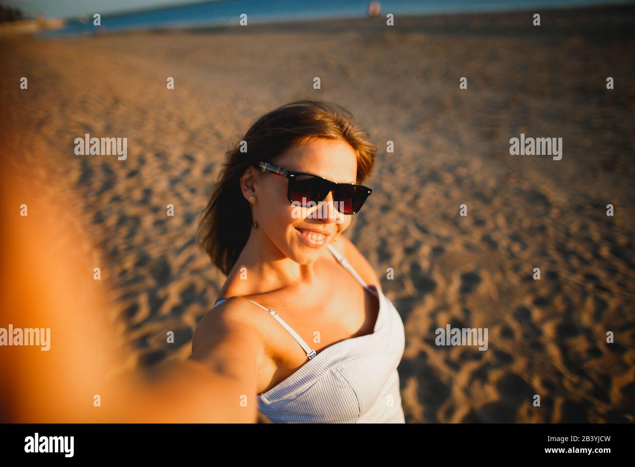 Belle femme bronzée prenant selfie sur la plage au coucher du soleil. Jolie  jeune femme en lunettes et robe sexy Photo Stock - Alamy