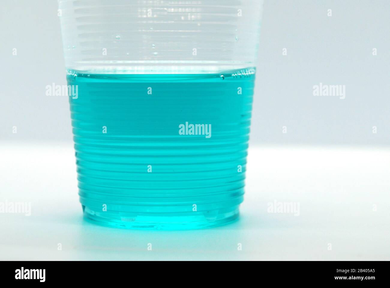 Fragment de tasse en plastique avec liquide de couleur bleu turc brillant sur fond blanc Banque D'Images