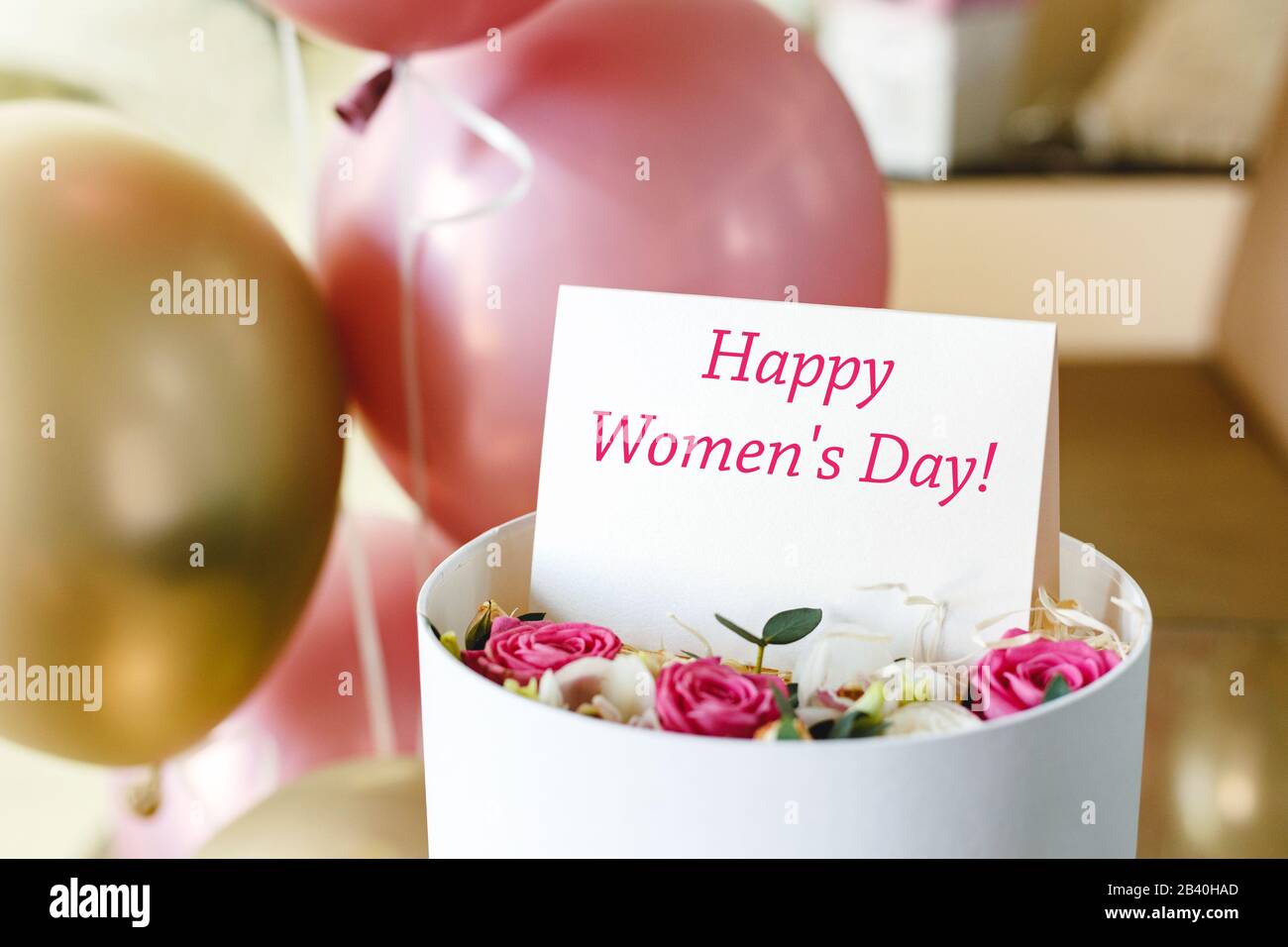 Happy Womens Day texte sur la carte-cadeau dans la boîte à fleurs près des roses festives et des ballons d'or. Carte de vœux pour les femmes le 8 mars, Journée internationale de la femme Banque D'Images