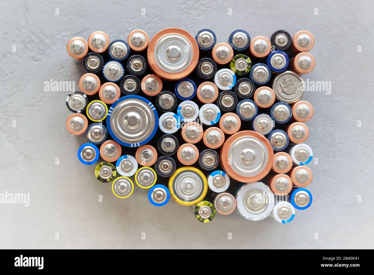 Gros plan sur les extrémités positives des batteries déchargées colorées de tailles et de formats différents, vue de dessus. Pile alcaline utilisée sur fond de béton. Haz Banque D'Images