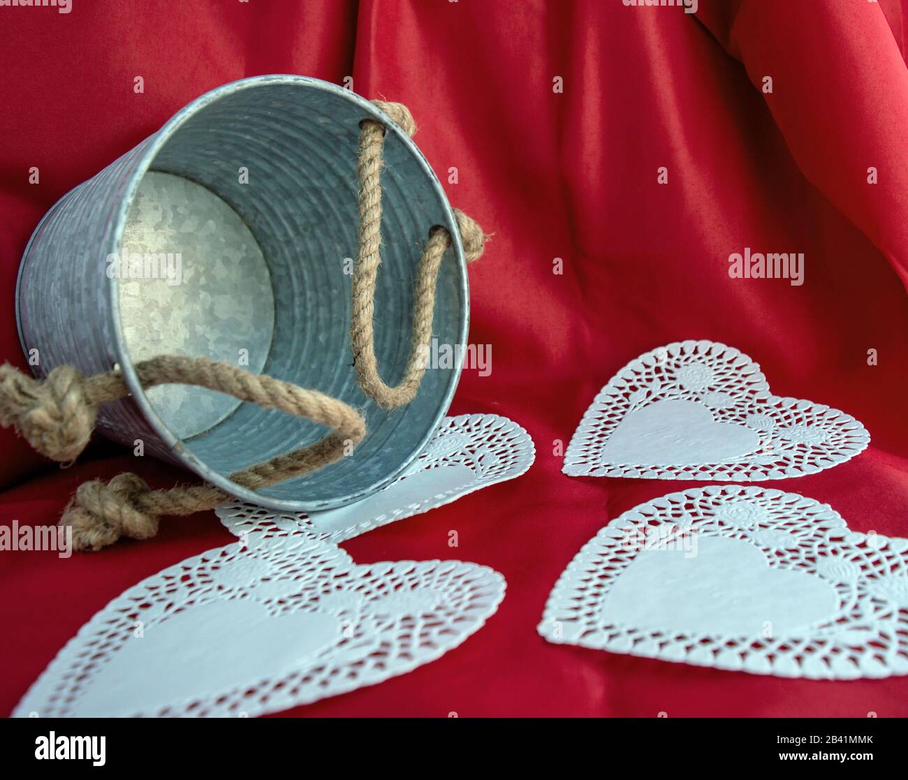 Un seau en étain, des poignées de corde, des coeurs blancs et un fond rouge doux représentant l'amour de la Saint-Valentin. Effet bokeh. Banque D'Images