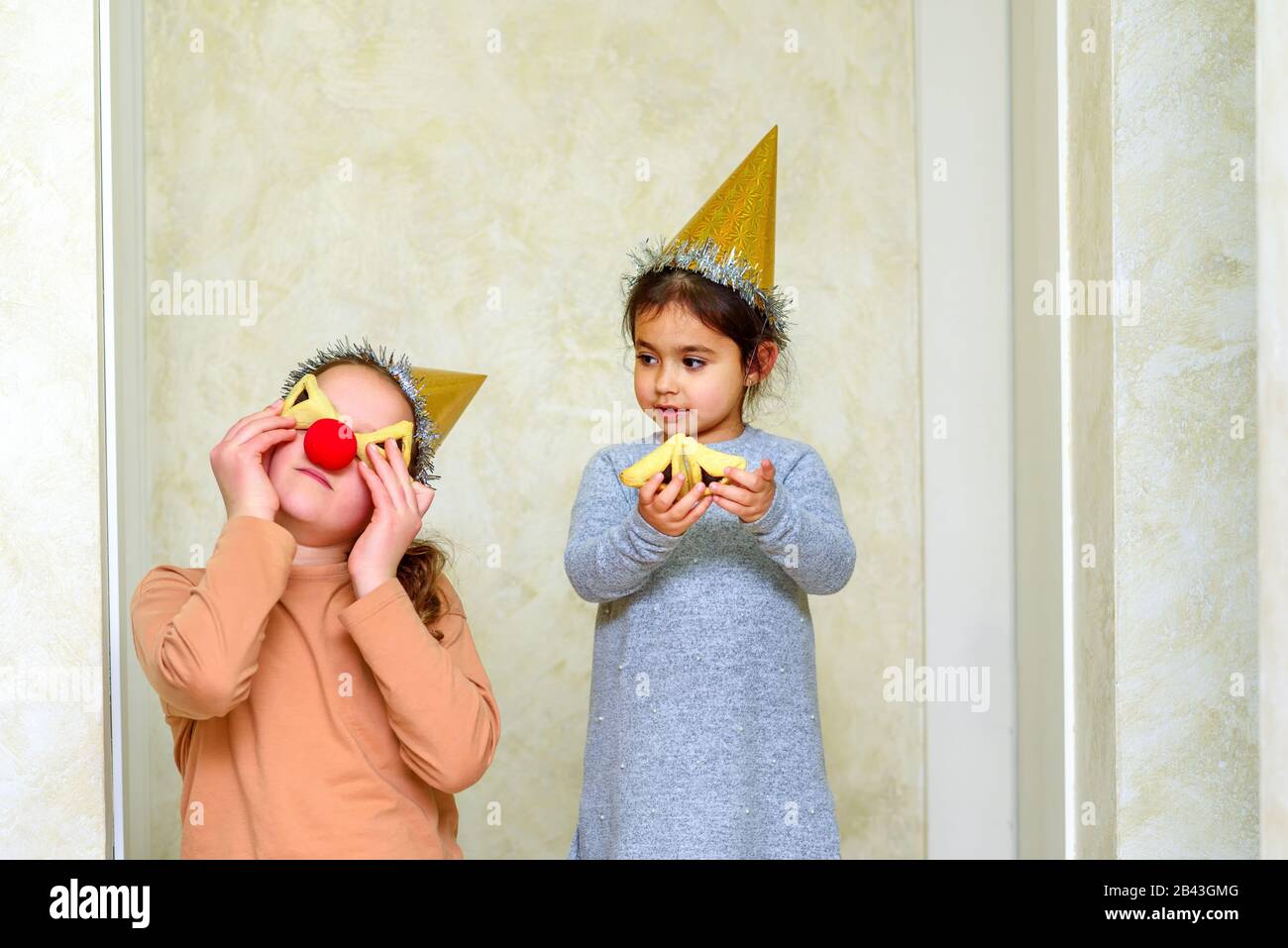Portrait d'une adolescente avec un nez clown s'amuser avec un petit enfant dans un chapeau de fête manger du hamantaschen, des cookies de triangle sur le Purim ou la fête d'anniversaire. Banque D'Images