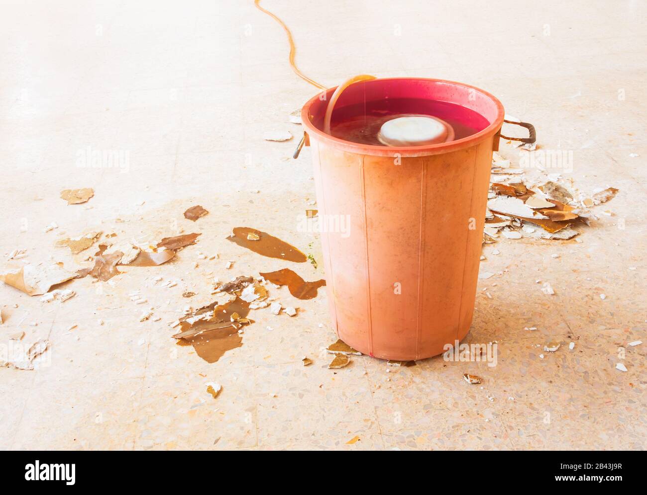 dépôt de fuite d'eau bâtiment intérieur de bureau dans le seau rouge du plafond de gypse et débit sur le sol en terrazzo Banque D'Images