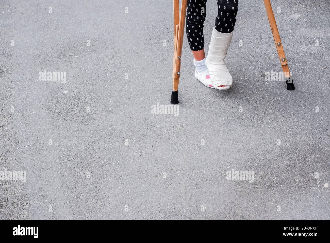 Enfant utilisant des béquilles et des jambes cassées pour marcher à l'extérieur, gros plan. Jambe cassée, béquilles en bois, blessure à la cheville. Fracture osseuse et fracture de la cheville BEI Banque D'Images