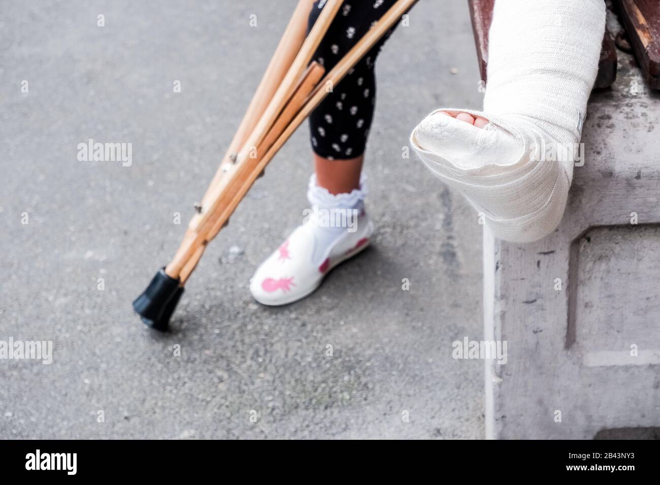 Enfant utilisant des béquilles et des jambes cassées pour marcher, un accident pendant les sauts. Jambe cassée, béquilles en bois, enfant avec jambe cassée en plâtre blanc moulé Banque D'Images