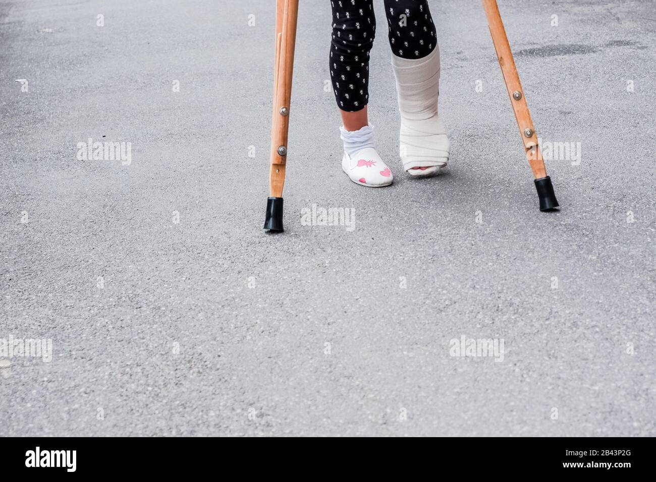 Enfant utilisant des béquilles et des jambes cassées pour marcher à l'extérieur, gros plan. Jambe cassée, béquilles en bois, blessure à la cheville. Fracture osseuse et fracture de la cheville BEI Banque D'Images