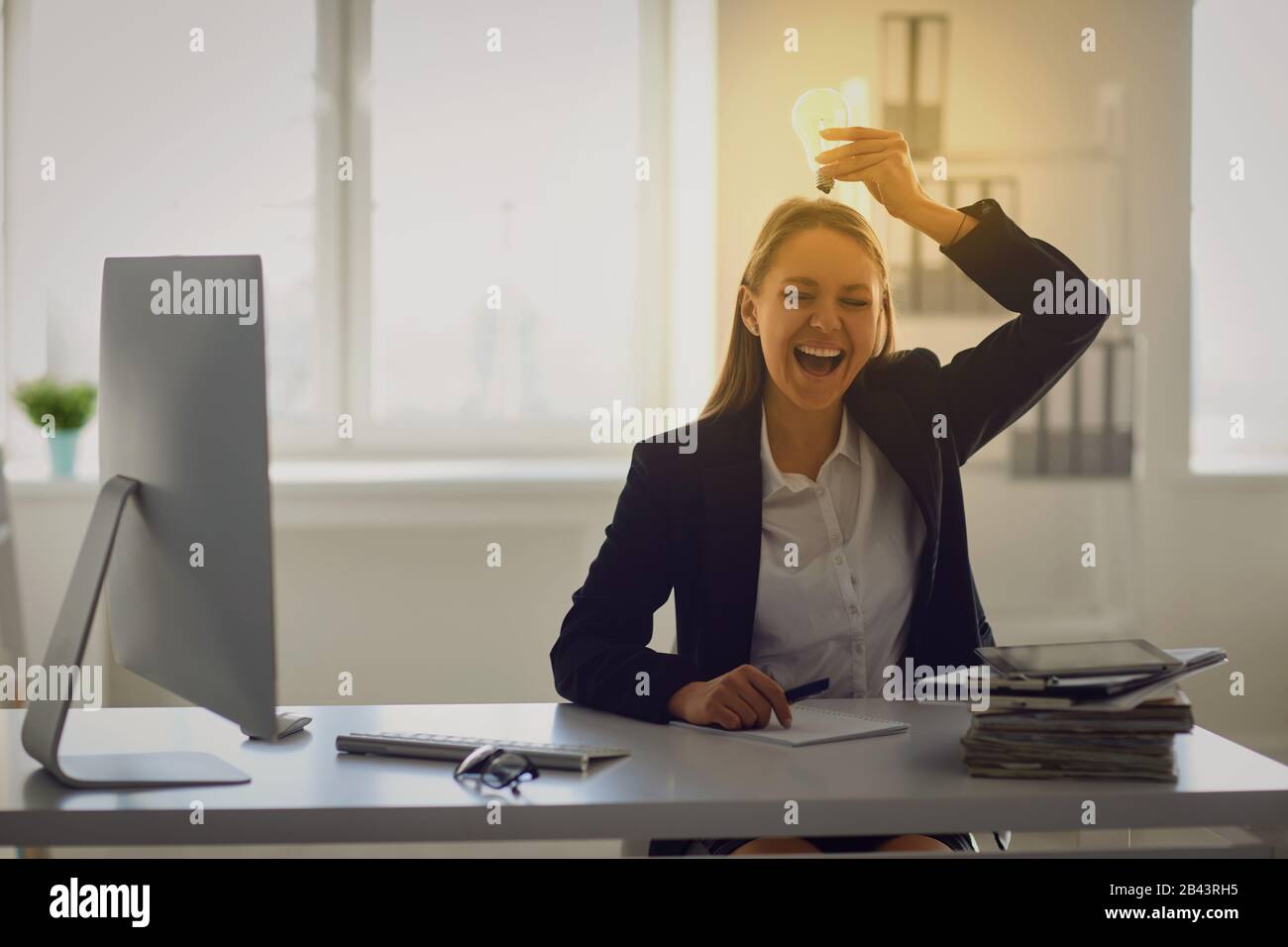 Une femme d'un costume d'affaires tient une lampe lumineuse dans ses mains à une table au bureau. Banque D'Images