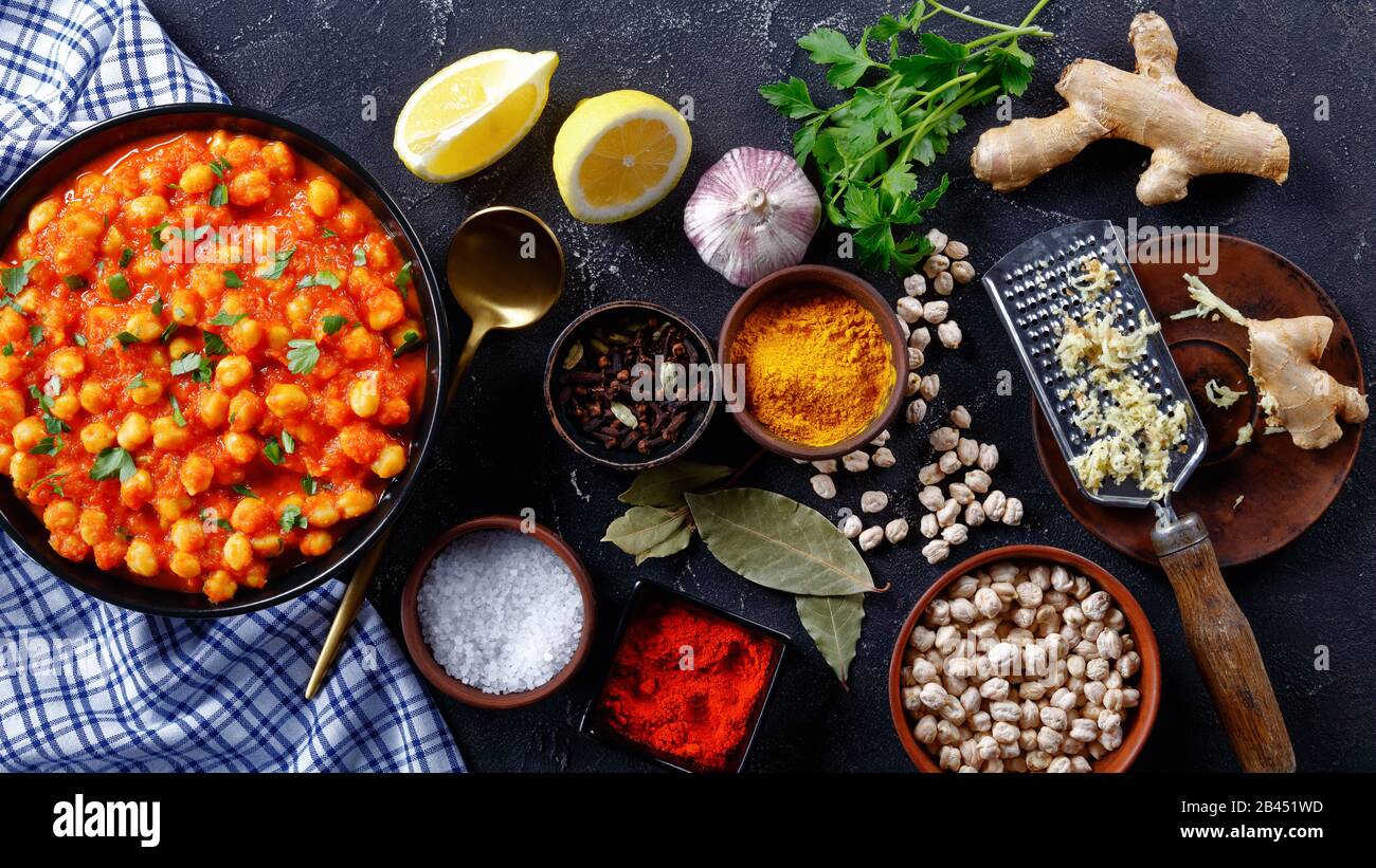 Curry épicé de pois chiches avec des ingrédients sur fond de béton foncé : curcuma, poudre de piment, gingembre, ail, gousses, laurier, sur une plaque noire avec l Banque D'Images