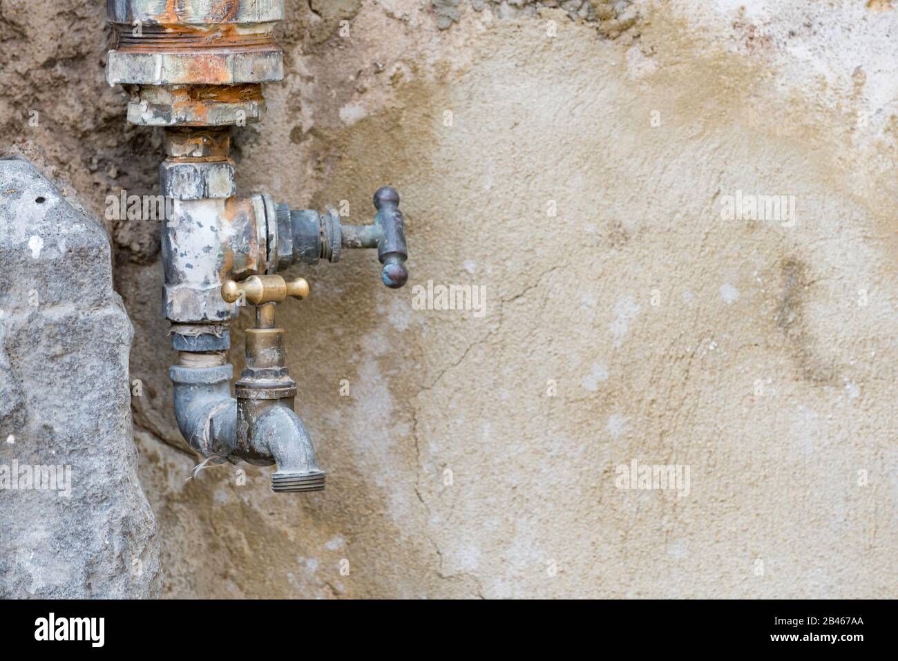 Un robinet extérieur double corrodé ou un robinet se fond presque dans le fond du mur derrière lui Banque D'Images