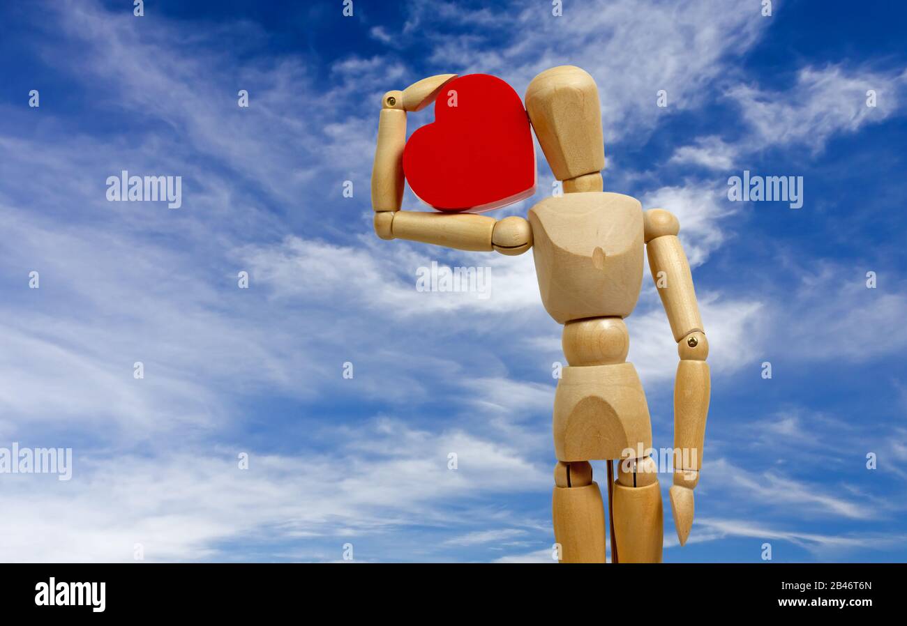 Mannequin humain en bois tenant un grand cœur rouge avec un ciel bleu comme arrière-plan Banque D'Images