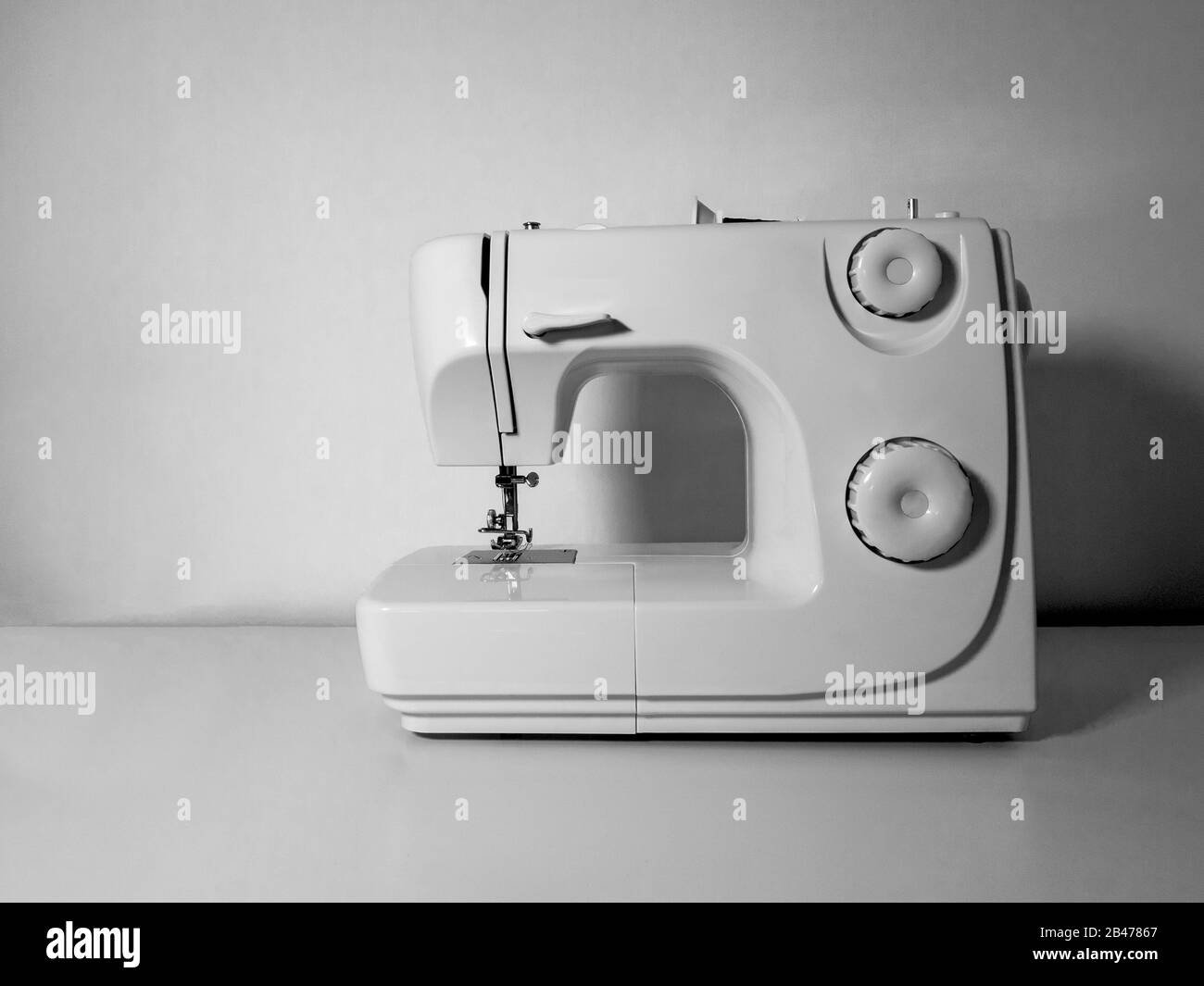 Machine à coudre vierge sur une table blanche et un fond de mur blanc. Image en noir et blanc. Concept d'artisanat. Banque D'Images