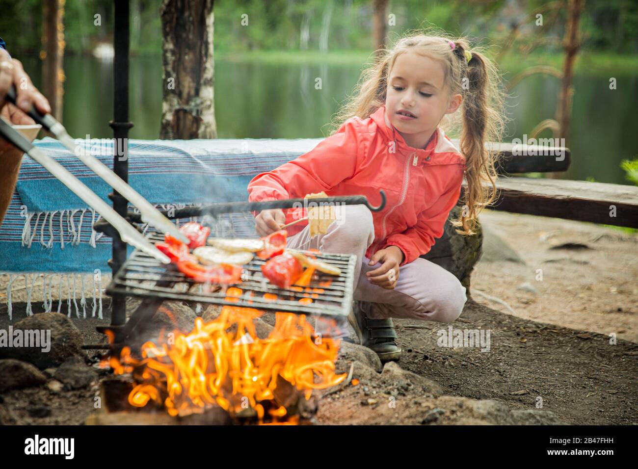 L'homme et sa petite fille ont barbecue dans la forêt sur la rive rocheuse du lac, faisant un feu, griller du pain, des légumes et des guimauves. Bonne Famille Banque D'Images
