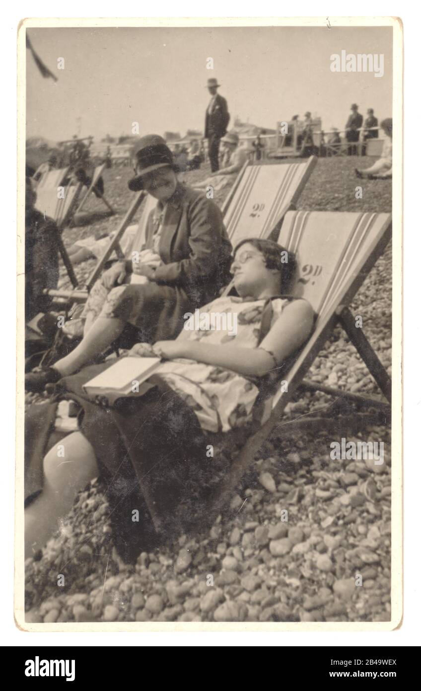 Début des années 1920, photo franche de femmes en transats, l'une endormie, l'autre riant de son amie. Au verso de la carte postale est écrit 'août 1928, Brighton' Brighton, Sussex, Angleterre, Royaume-Uni rétro photo de plage Banque D'Images