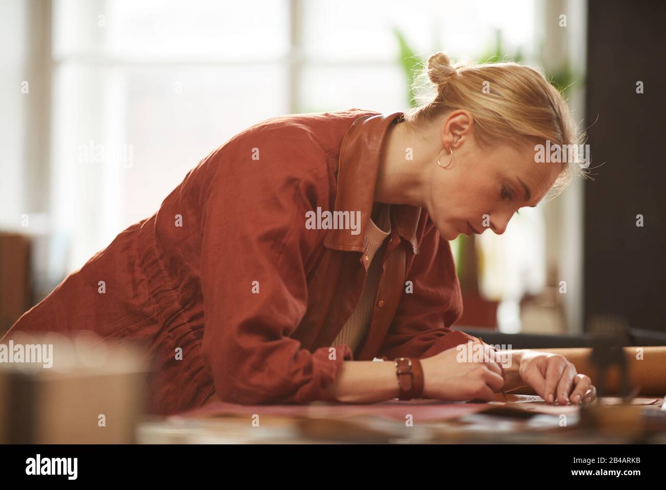 Portrait horizontal moyen de belle femme caucasienne avec cheveux blonds travaillant dans son atelier d'artisanat en cuir Banque D'Images