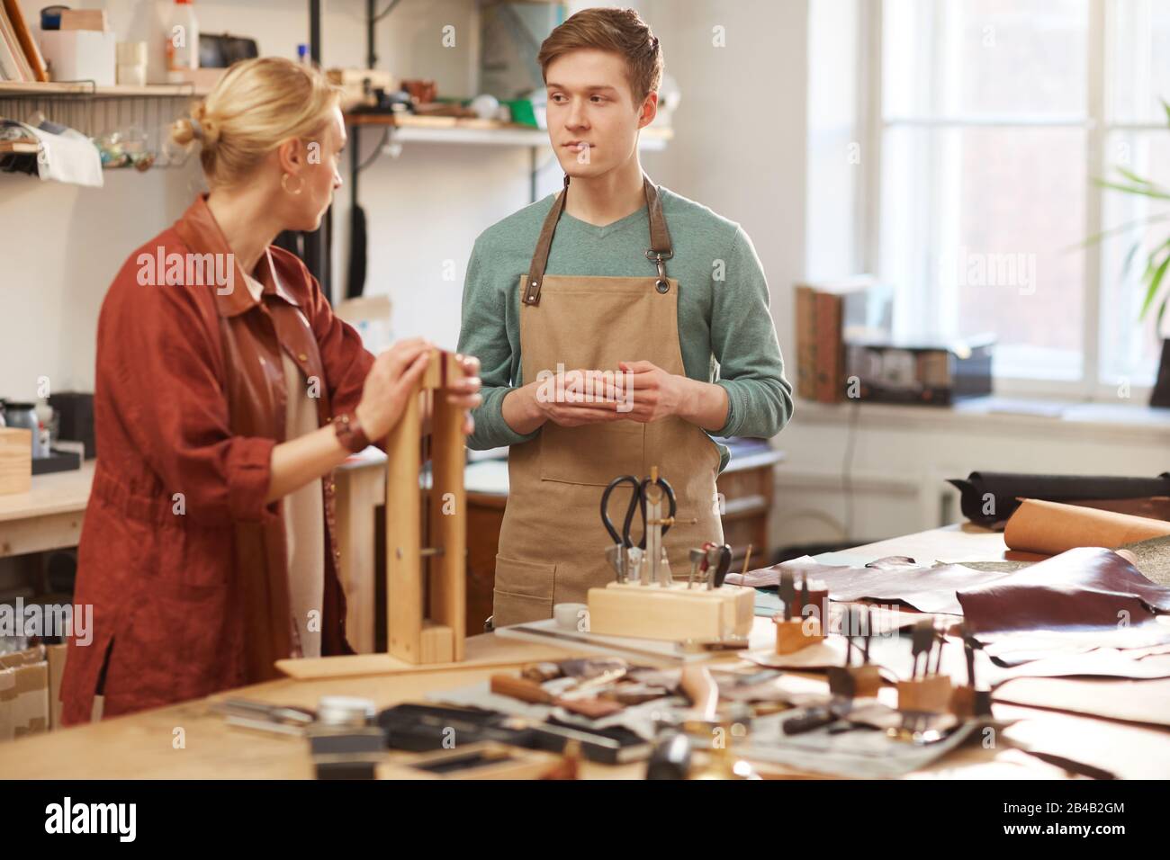 Artisan féminin caucasien démontrant à son apprenti comment utiliser le clip en bois d'artisanat en cuir, photo horizontale Banque D'Images