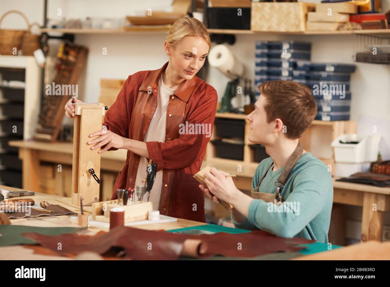 Deux jeunes artisans discutant tout en travaillant ensemble dans un atelier moderne d'artisanat en cuir, photo horizontale Banque D'Images