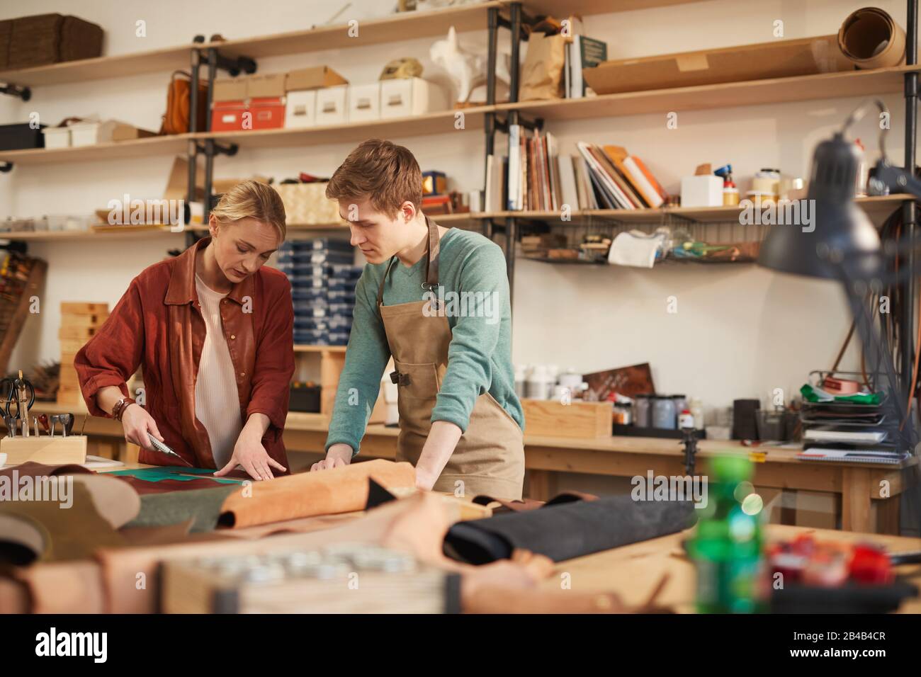 Jeune homme attentif et femme concentrée créant ensemble un nouvel artisanat en cuir dans un atelier moderne Banque D'Images