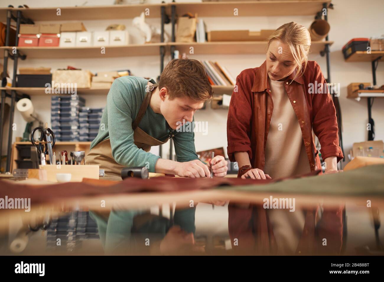 Photo horizontale de deux jeunes hommes et femmes concentrés travaillant ensemble dans un atelier moderne d'artisanat en cuir Banque D'Images