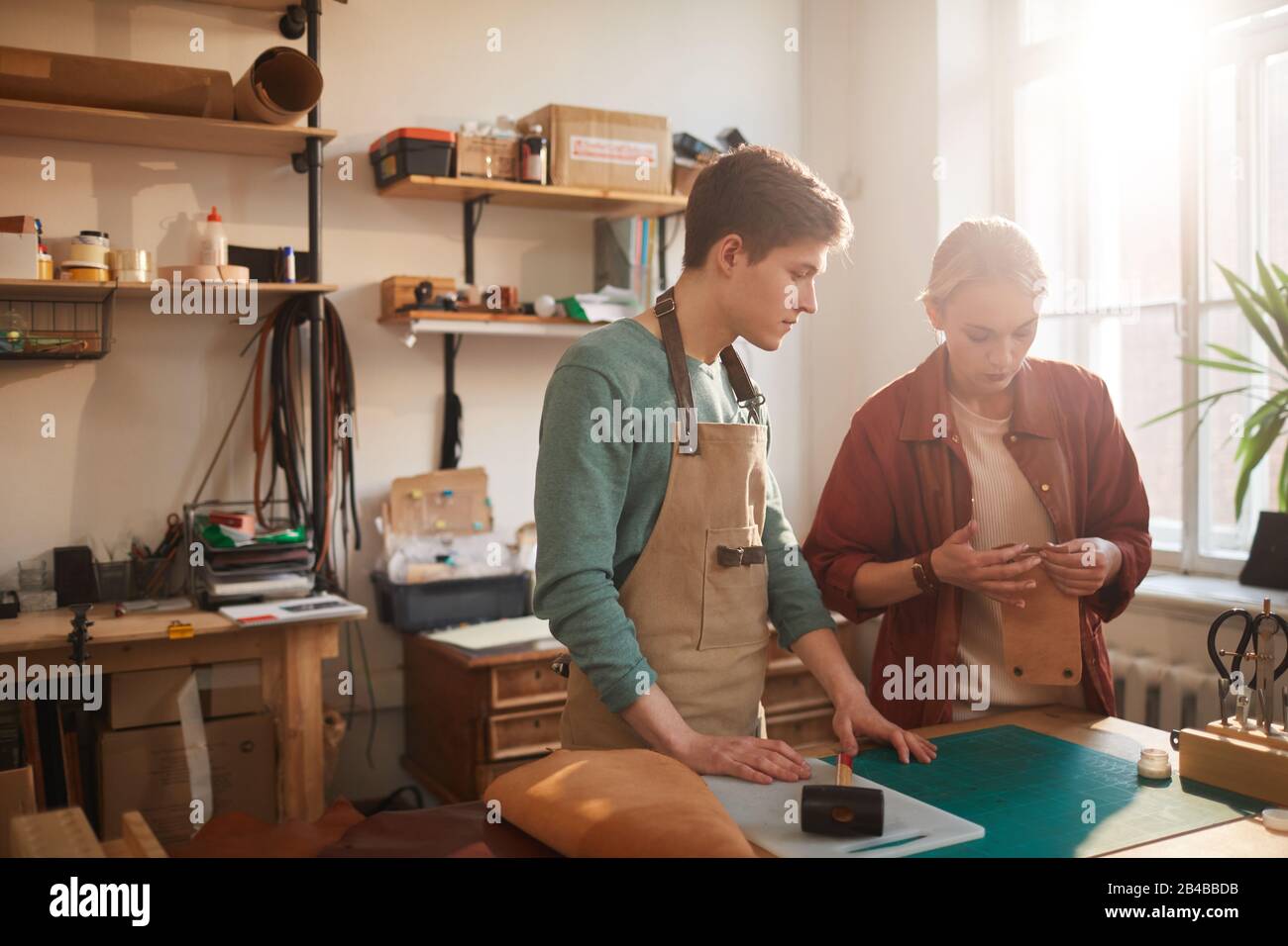 Photo horizontale de deux jeunes artisans debout à la table d'atelier pour vérifier la qualité des détails des nouveaux produits artisanaux en cuir, espace de copie Banque D'Images