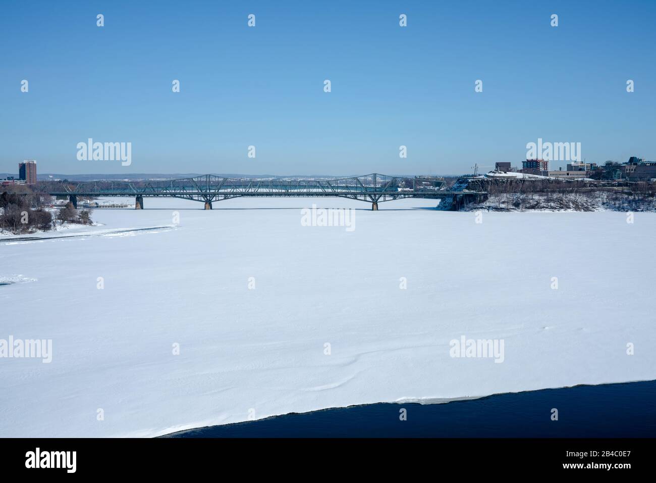 La rivière des Outaouais, encore gelée et recouverte de neige fraîche, commence à décongeler aux bords, signe du printemps sur son chemin. Banque D'Images