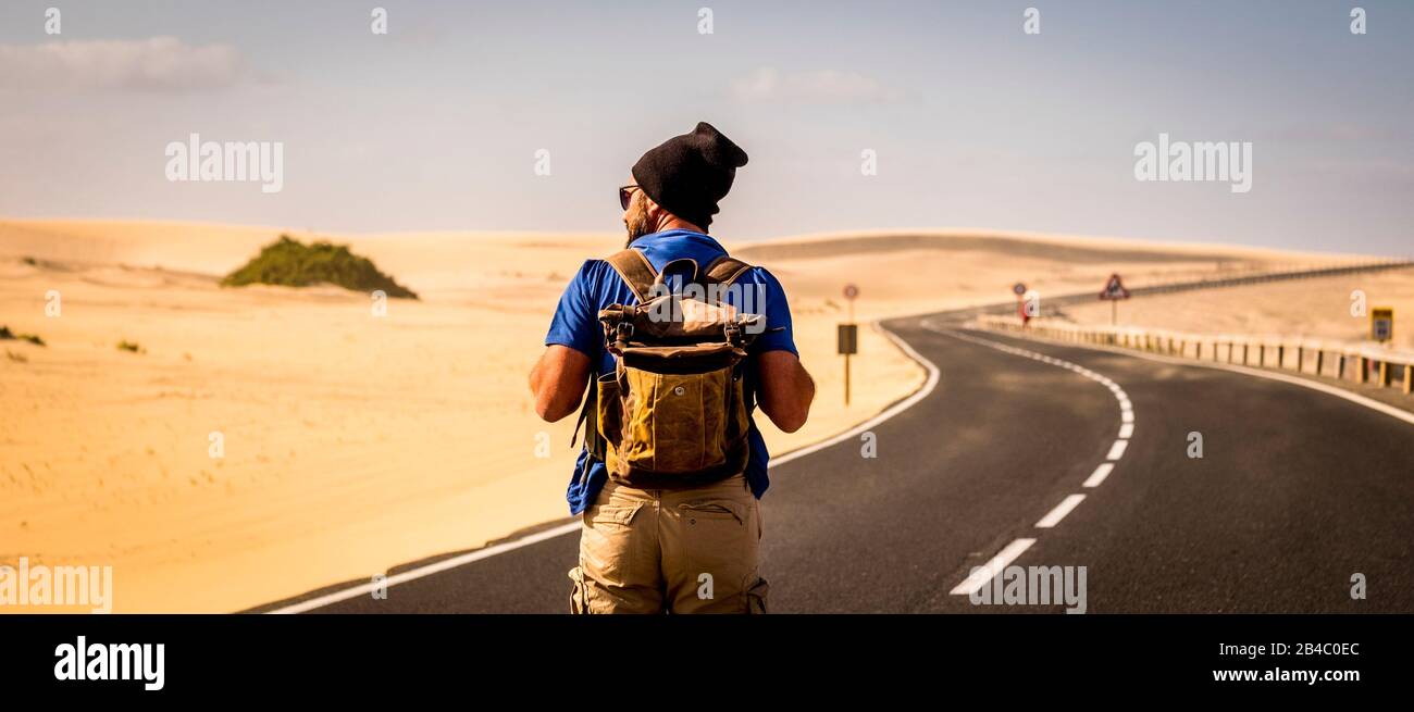 Image colorée de l'homme avec sac à dos de voyage marche au milieu de la route avec des dunes du désert autour - concept de voyageur alternatif pour les vacances d'été ou le style de vie au bonheur Banque D'Images