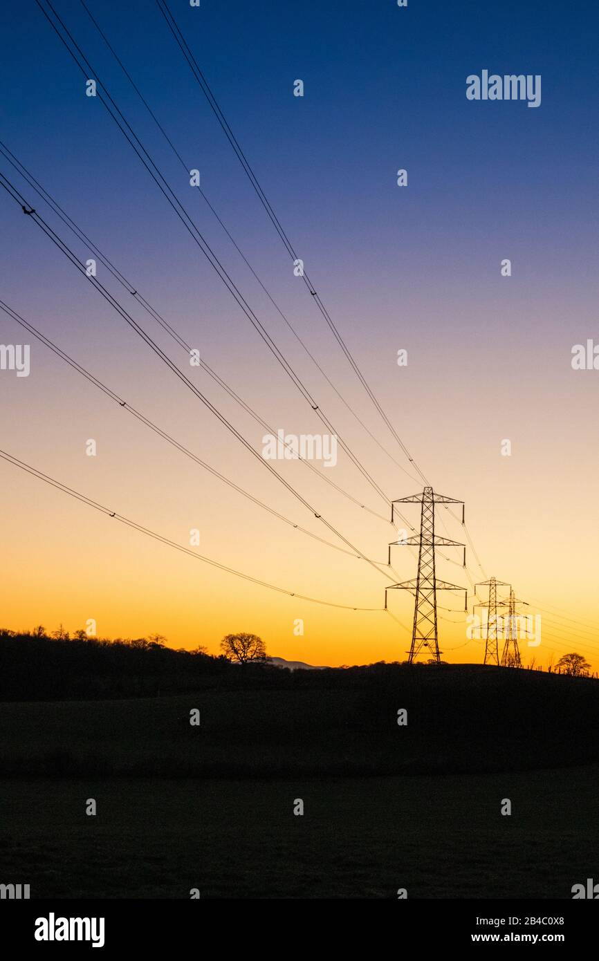 Un coucher de soleil hivernal derrière les lignes électriques et les pylônes à Milton près de Brampton, Cumbria Royaume-Uni Banque D'Images