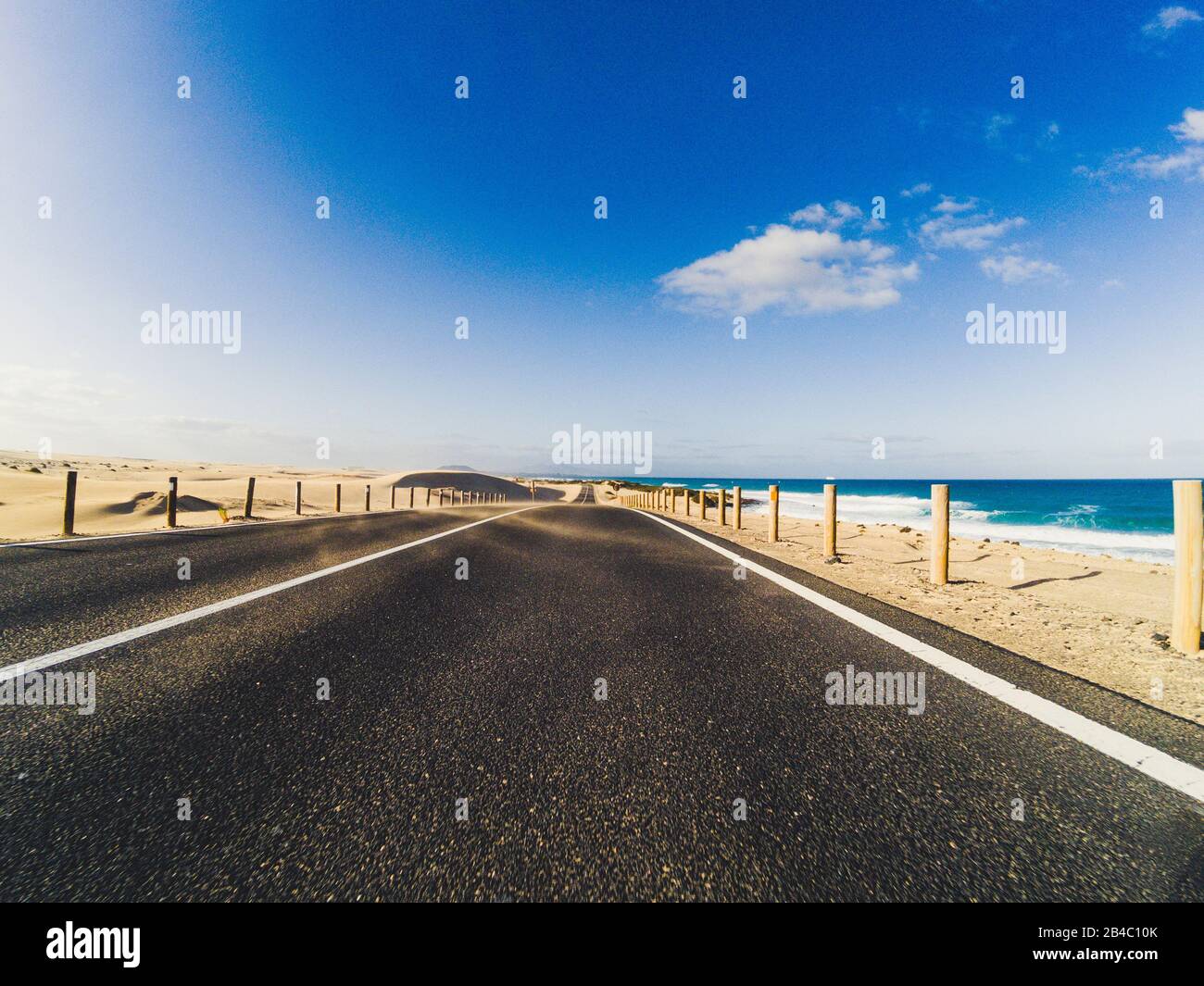 Route à long chemin pour le concept de transport de voiture de voyage avec désert et plage sur le côté - eau de mer et ciel bleu clair en arrière-plan - effet de mouvement Banque D'Images