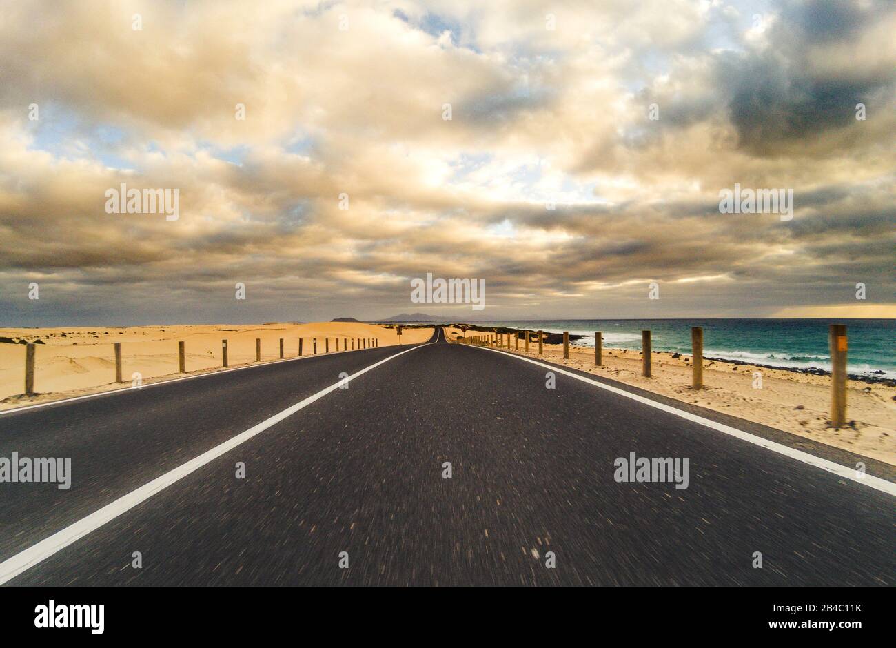 Route à long chemin pour voyage concept de transport de voiture avec désert et plage sur le côté - eau de mer et ciel nuageux magnifique en arrière-plan - effet de mouvement Banque D'Images