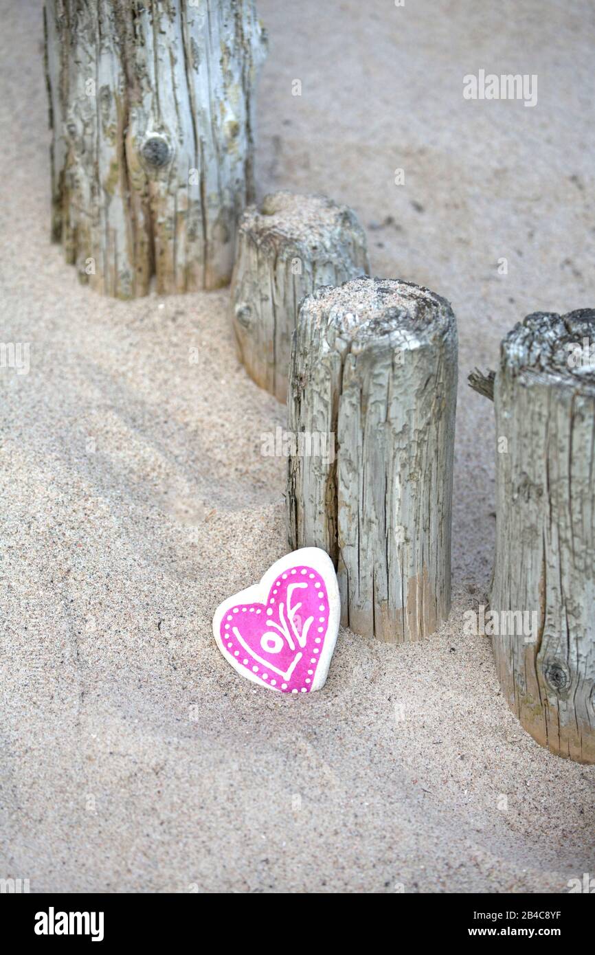Coeur en pierre rose avec amour de mot penchant sur des poteaux en bois weathered sur une plage de sable Banque D'Images
