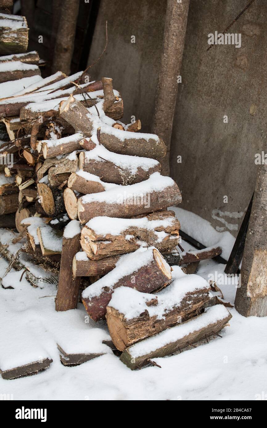 tas de bois de chauffage recouvert de neige devant une grange Banque D'Images