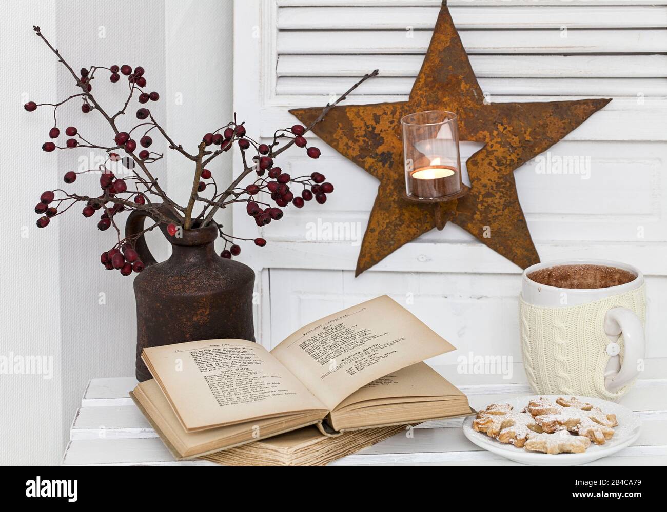 Un déocrement rustique d'hiver ou de Noël dans un intérieur blanc, avec des brindilles de baies rouges dans un vase, de vieux livres, du chocolat chaud et un porte-bougie en forme d'étoile Banque D'Images