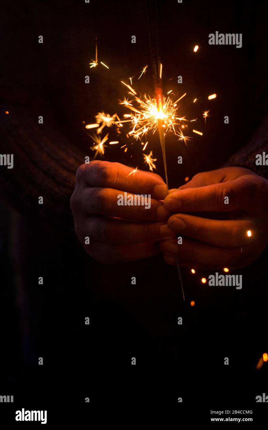 Image conceptuelle de Noël et de la veille du nouvel an avec une paire de mains de l'homme prenant un feu rouge parciant pour célébrer la fête de nuit - se concentrer sur les feux d'artifice et l'espoir pour les personnes futures Banque D'Images
