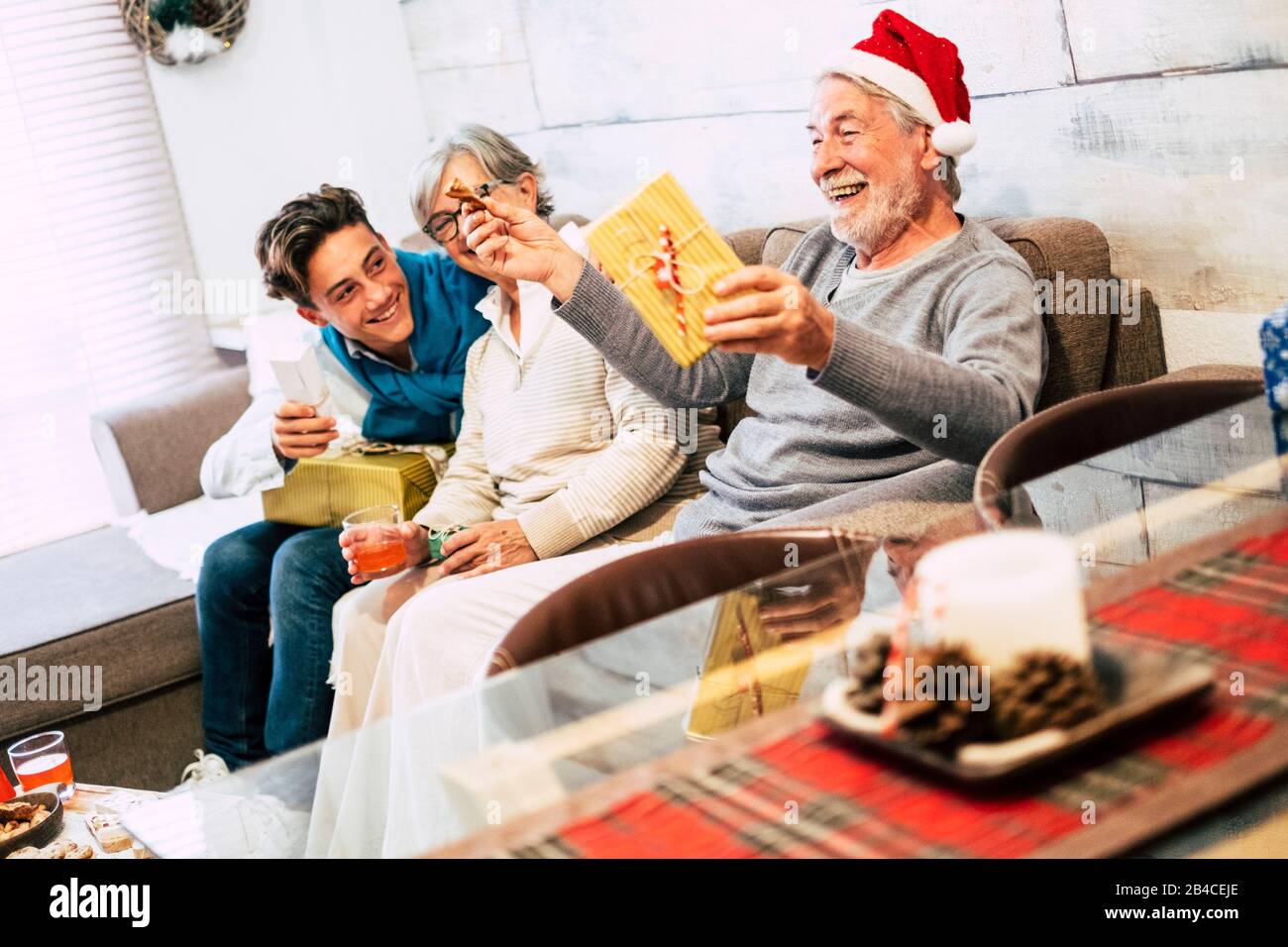 famille avec adolescent et grand-père assis au canapé à la maison le matin de noël rire et ouvrir leurs cadeaux avec beaucoup d'amour et d'affection - vacances conceps Banque D'Images