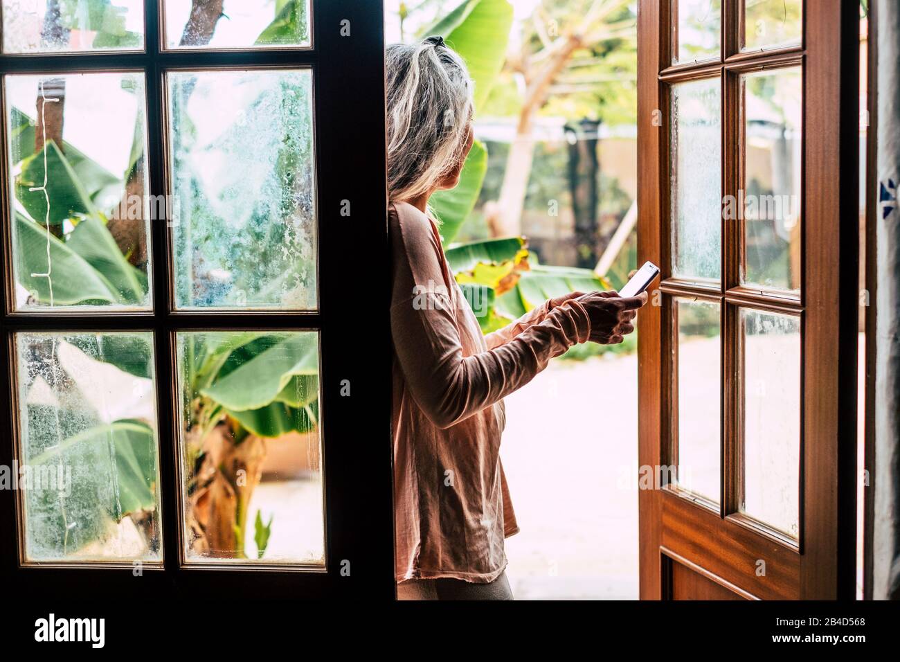 Beau style ancien vintage portrait de femme senior alternative dactylographie et lecture d'un appareil de téléphone mobile à la maison en dehors de la porte - les gens et la technologie dans la vie réelle Banque D'Images