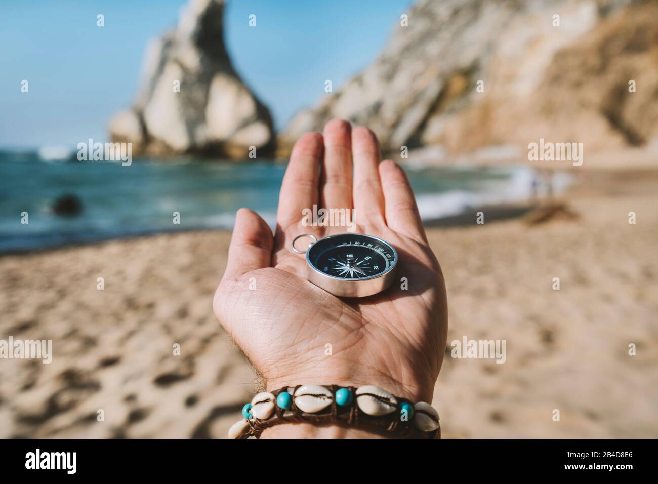 Main d'homme avec compas symbolisant le concept de recherche d'aventure contre la plage d'Ursa, Sintra, Portugal. Banque D'Images