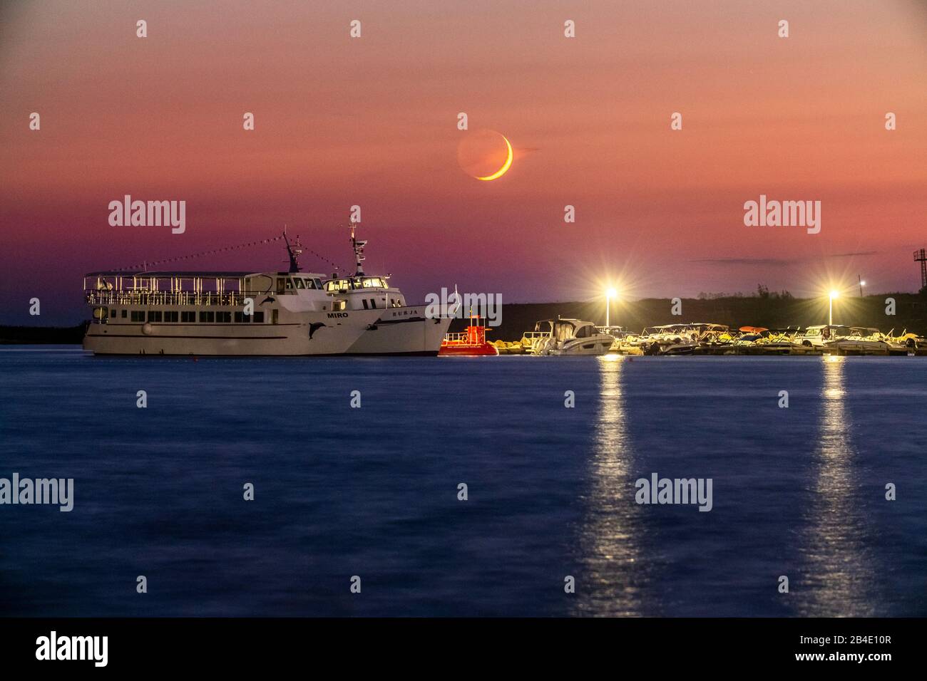 Nouvelle lune dans le ciel rouge au-dessus de la mer. Au premier plan, un navire. Banque D'Images