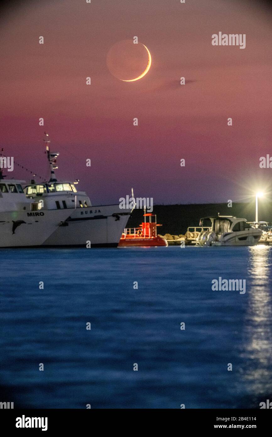 Nouvelle lune dans le ciel rouge au-dessus de la mer. Au premier plan, un navire. Banque D'Images