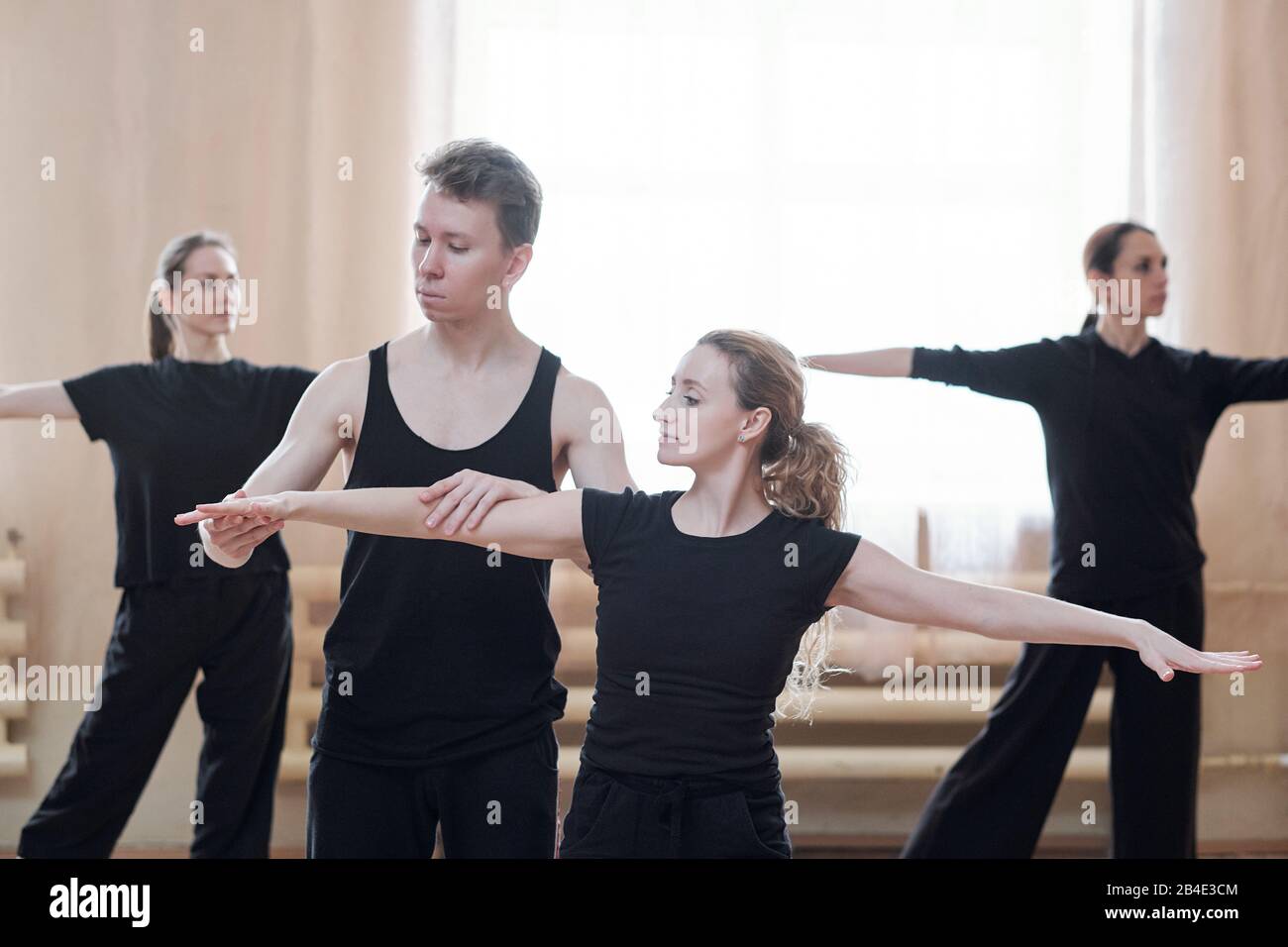 Jeune instructeur masculin de danse aider une des femmes avec des bras étirés pendant l'entraînement en studio moderne Banque D'Images