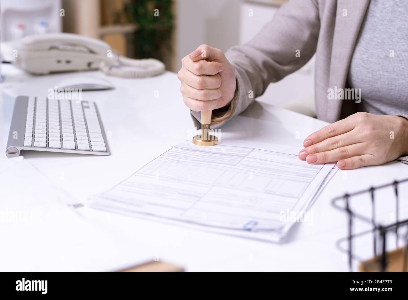 Les mains de la jeune employée de bureau assis à la réception et mettant le sceau sur le document financier avant de l'envoyer au client Banque D'Images