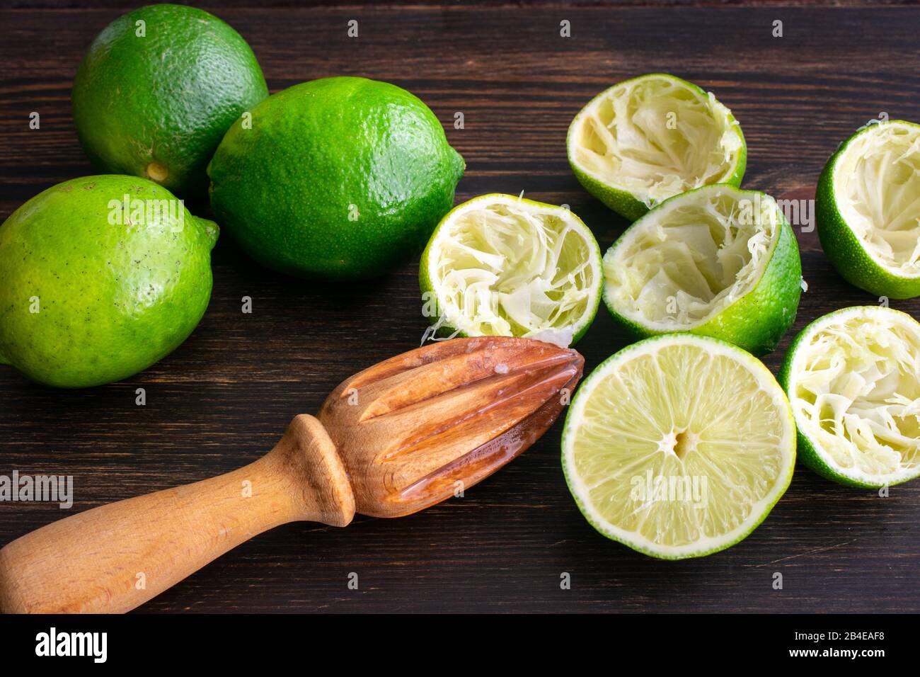 Limes juteux sur un tableau De Découpe du bois : moitiés de chaux et un presse-agrumes sur fond de bois sombre Banque D'Images