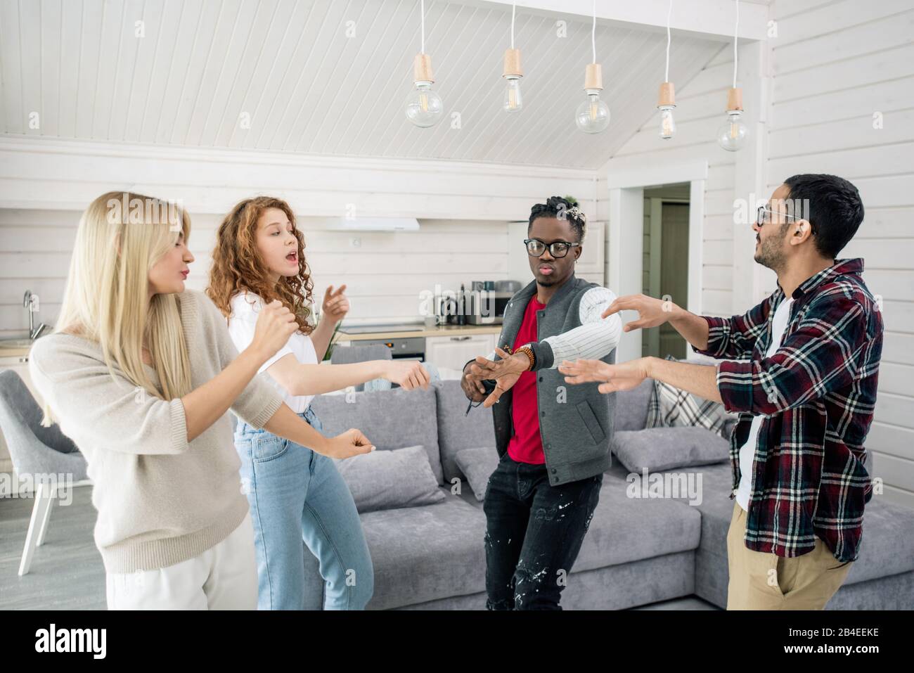 Deux jeunes couples interculturels qui dansent ensemble dans la salle de séjour à la maison sur fond de canapé et de cuisine Banque D'Images