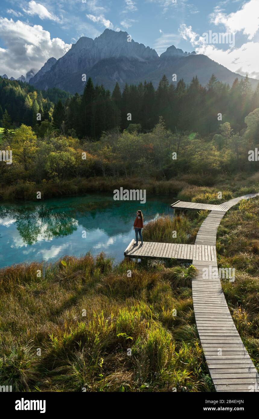 Réserve naturelle de Zelenci en Slovénie. Photo portrait d'une fille debout près d'un lac aux eaux cristallines et regardant les Alpes. Banque D'Images