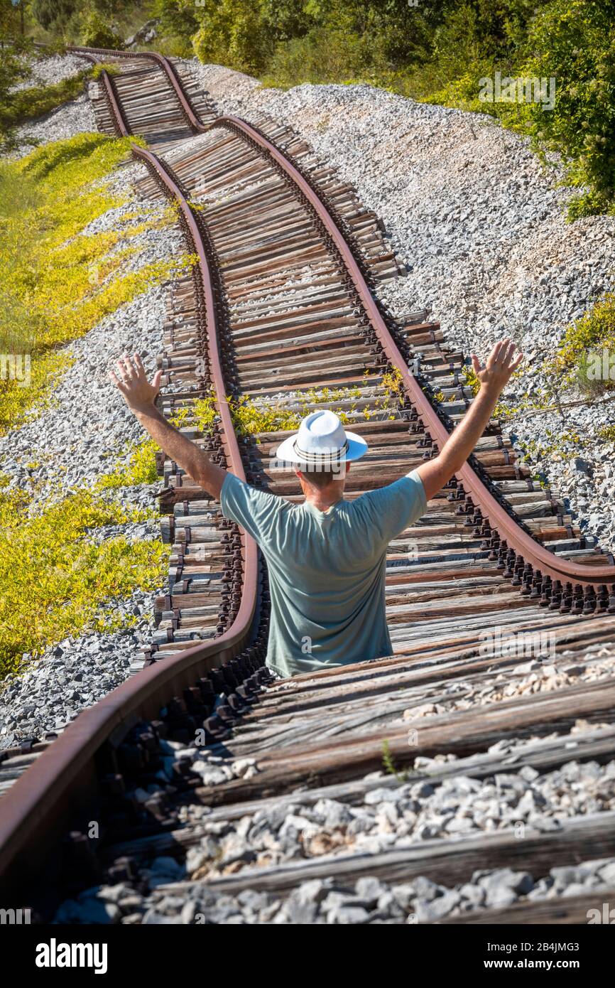 L'homme avec un chapeau blanc au milieu de rails abandonnés semble vouloir arrêter un train imaginaire, Pijana pruga, Kozljak, Krsan, Istrie County, Croatie Banque D'Images